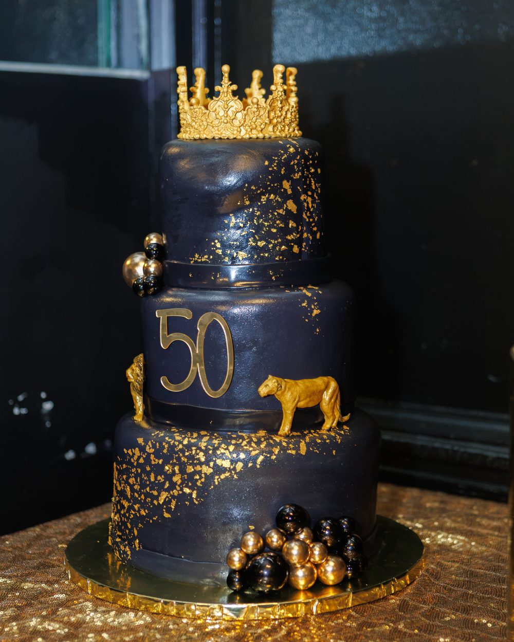 Three-tier black and gold 50th birthday cake with lion and crown details