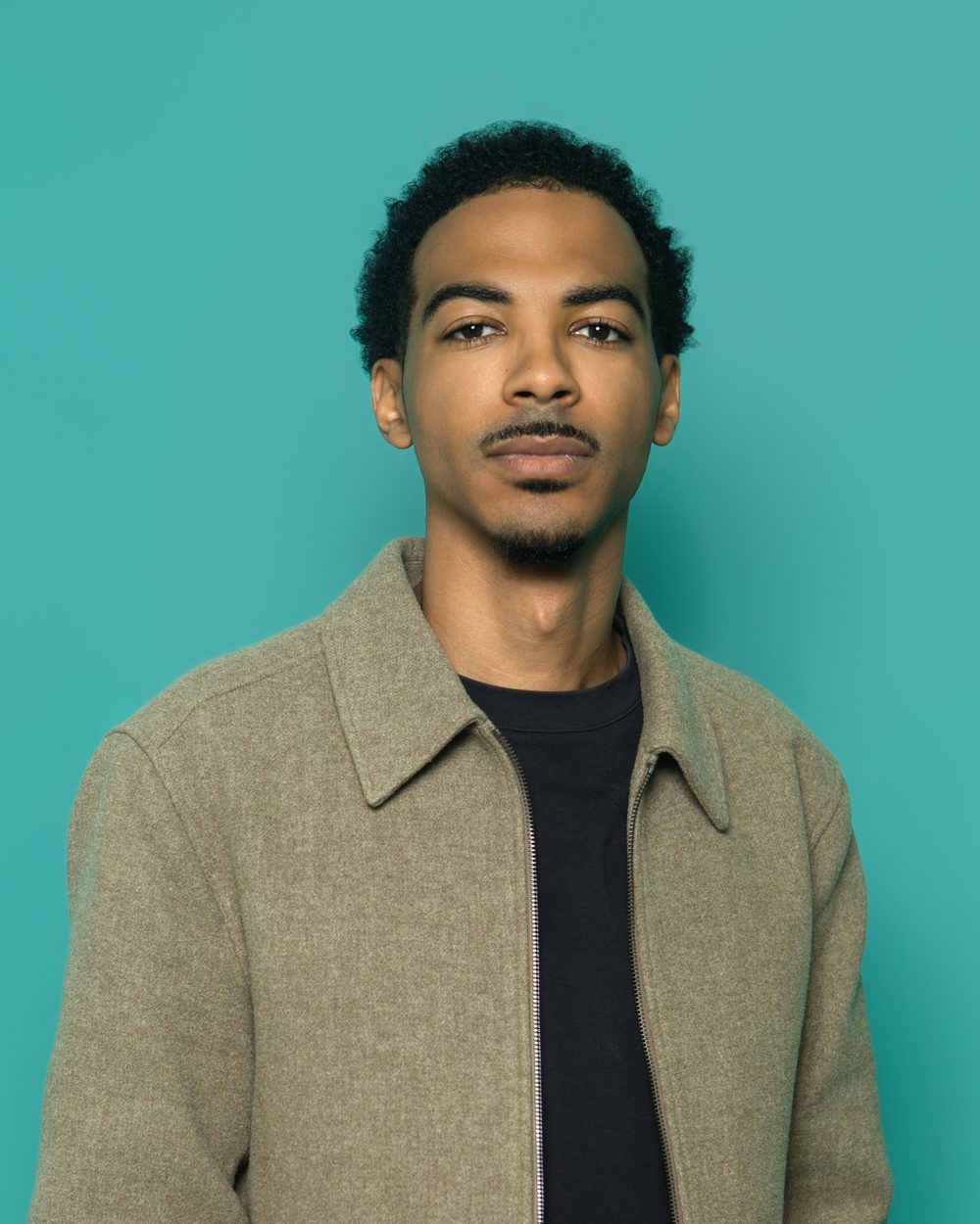 Corporate headshot, serious expression, olive jacket