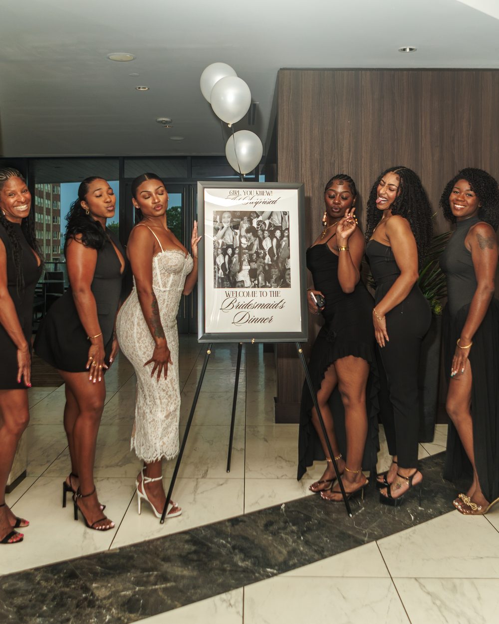 Bridesmaids gathered around a surprise reveal sign, laughing